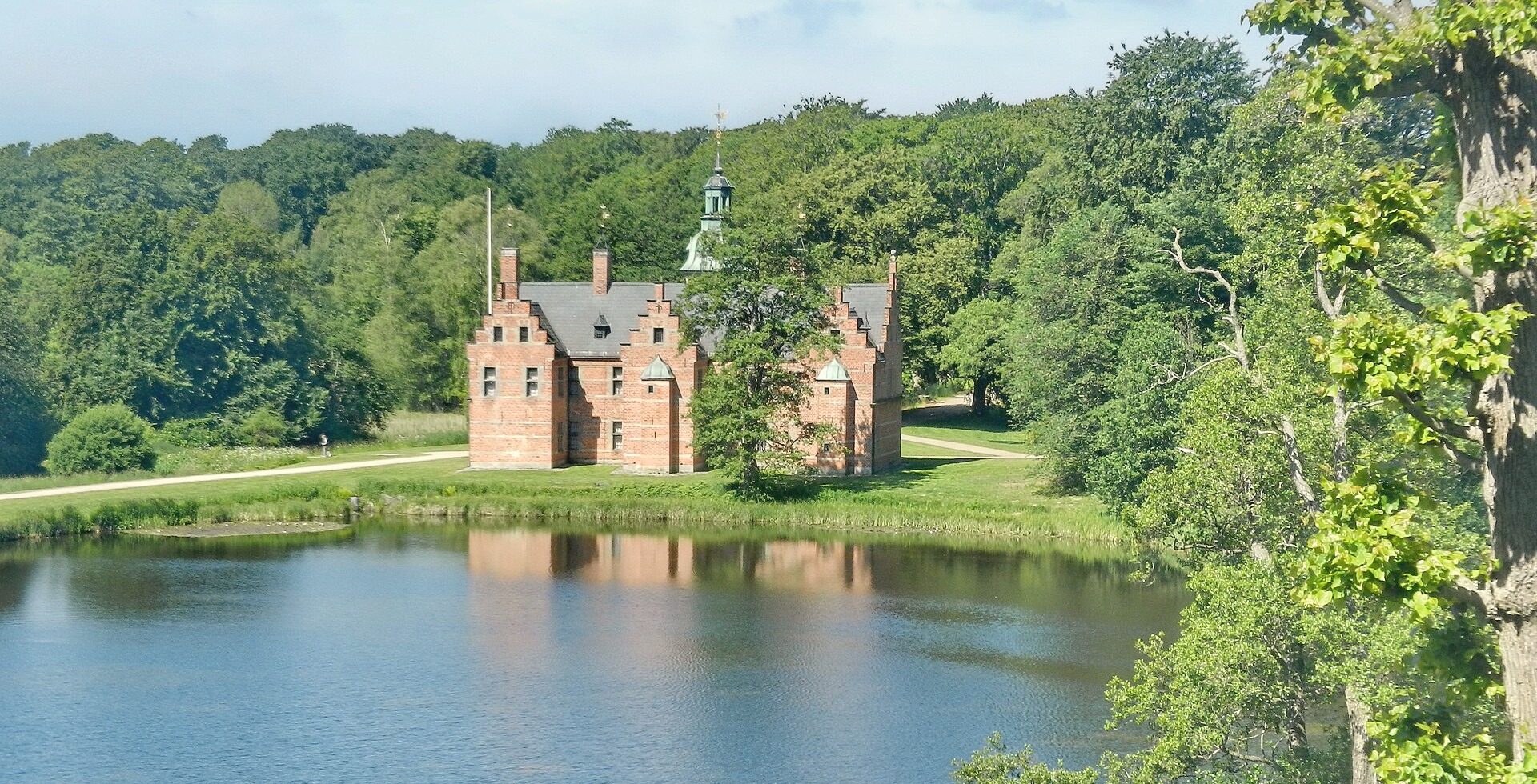 Badstueslottet ved Slotssøen i Hillerød om sommeren med blå himmel, solskin og roligt vand